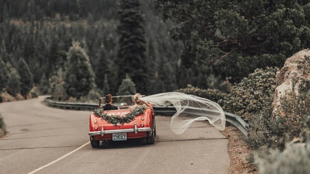 Bride and groom drive away in a red convertible get away car