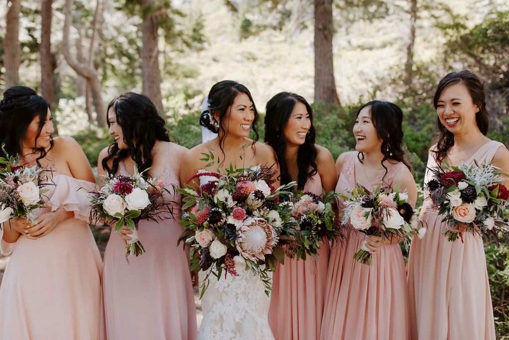 Asian bride and her bridesmaids wearing blush bridesmaid dresses while holding maroon and different shades of pink and peach bouquets
